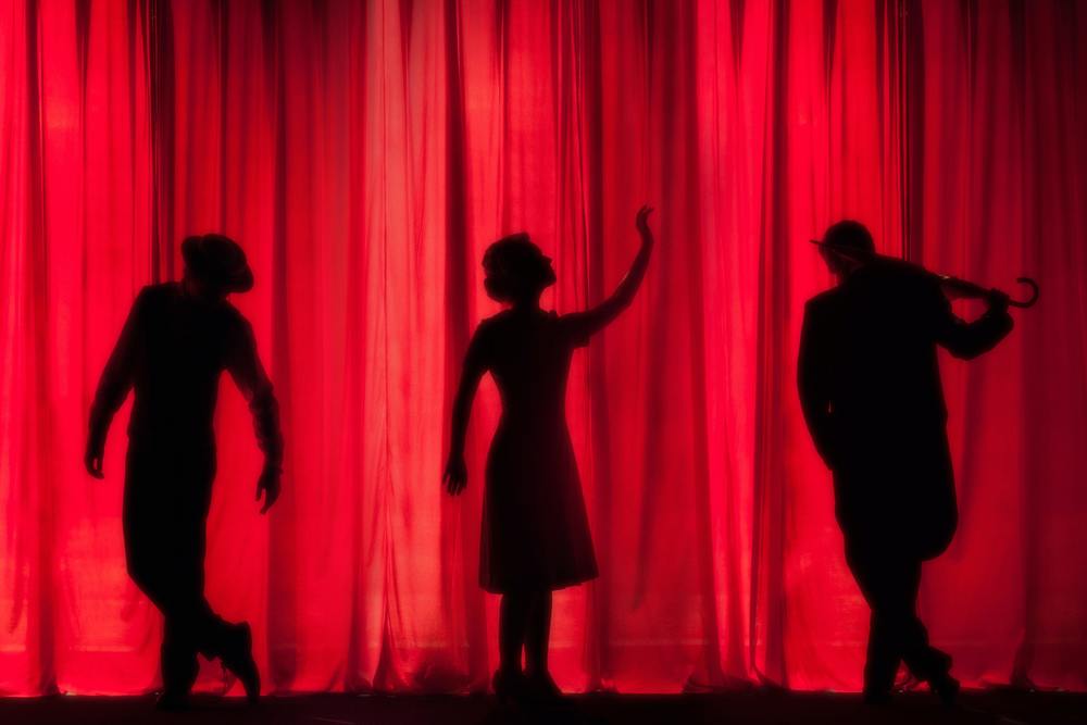 Silhouettes of performers behind red curtain